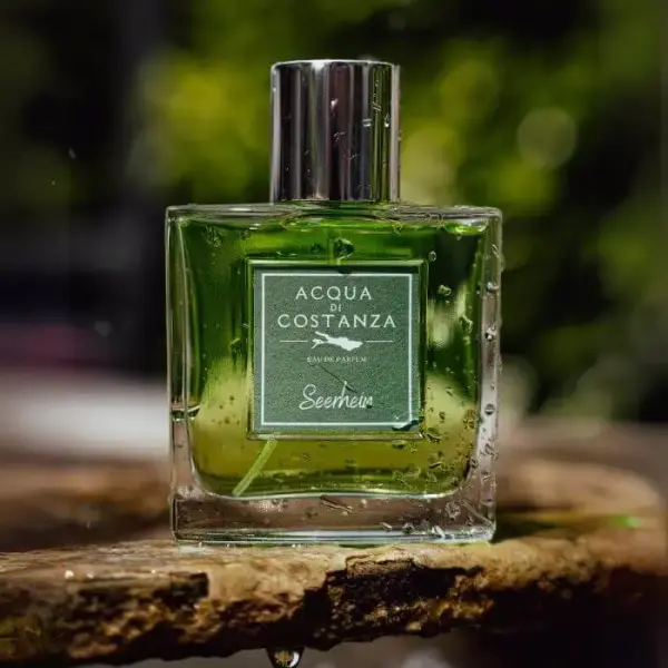 Acqua di Costanza Seerhein Unisex Parfum Flakon mit Wassertropfen auf einer feuchten Holz- oder Steinoberfläche, grüner Duft vor unscharfem Grün im Hintergrund.