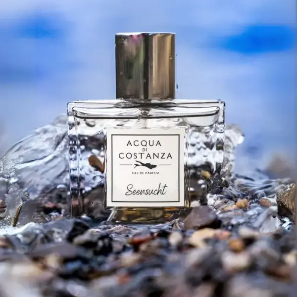 Acqua di Costanza Seensucht – Unisex Eau de Parfum im transparenten Flakon, fotografiert zwischen Wasser und Steinen am Ufer des Bodensees.